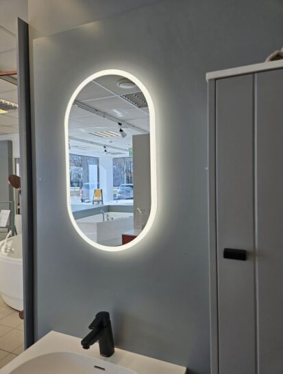 O-Series oval LED mirror mounted on a showroom wall in a bathroom display setting.